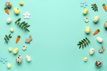 Frame made of green leaves, Easter eggs and decorative flowers on turquoise background