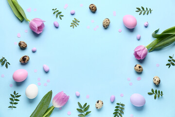 Frame made of Easter eggs, green leaves and flowers on blue background