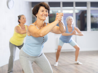 Cheery elderly woman engaged in dancing in fitness studio together with other attendees