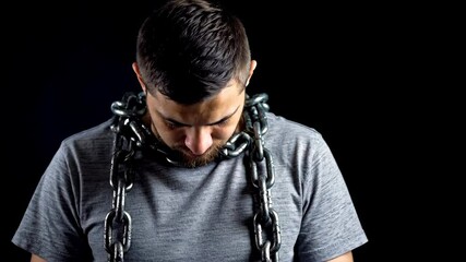 Young man with a chain around his neck, looking down, dark background, captive concept