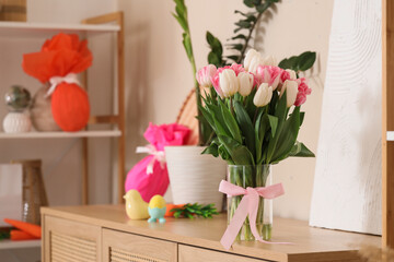 Vase of beautiful tulip flowers with Easter decorations on commode in festive living room