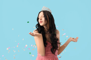 Beautiful happy teenage girl in stylish pink prom dress and tiara with confetti blowing kiss on...