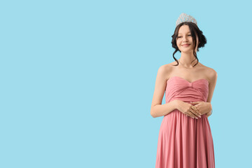 Beautiful happy teenage girl in stylish pink prom dress and tiara on blue background