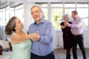 Obraz premium Senior man and elderly woman are dancing classic version of waltz in couple during lesson at studio. Leisure activities and physical activity for positive people.