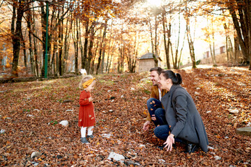 Fototapeta premium Little girl stands in front of smiling mom and dad squatting in the forest