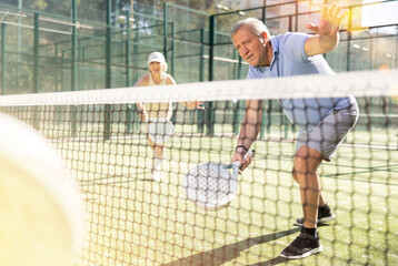 Motivated senior man playing padel with his teammate in court