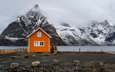 Traditional yellow rorbu house and Olstinden mountain peak in Sakrisoy fishing village, Lofoten, Norway