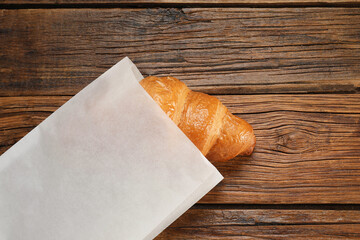 Paper bag with fresh croissant on wooden table, top view