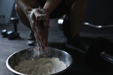 Woman applying talcum powder onto her hands above bowl before training in gym, closeup