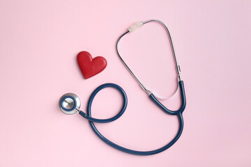 Cardiology. Stethoscope and red decorative heart on pale pink background, flat lay