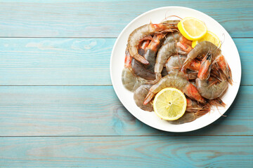 Fresh raw shrimps with lemon on light blue wooden table, top view. Space for text