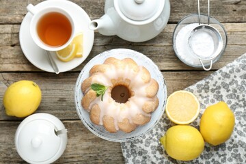 Tasty lemon cake with glaze, tea and fresh fruits on wooden table, flat lay