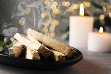 Palo Santo stick smoldering and burning candles on grey table, closeup