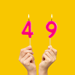 Hands holding birthday candles with number 49 - Yellow background