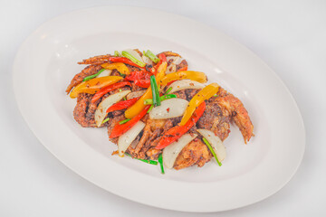 A plate of crispy soft-shell crab stir-fried with bell peppers, onions, and scallions, served with a savory sauce for a flavorful and colorful dish.