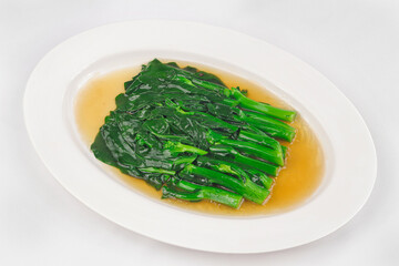 A plate of stir-fried Chinese kale in a light brown sauce, served on a white oval dish, with vibrant green color and a glossy texture.
