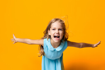 Joyful little girl in blue dress excitedly jumping against vibrant orange background