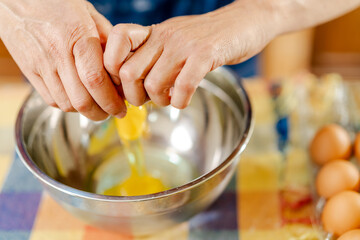 Chef cracking eggs into metal bowl for baking recipe