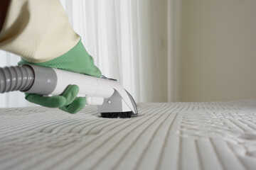 Cleaning a bed mattress with a steam cleaner in a bright room