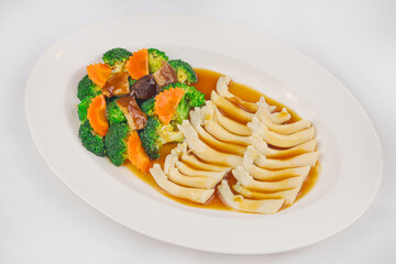 A dish of sliced bamboo shoots in a savory sauce, served with stir-fried broccoli, carrots, and mushrooms, garnished for an elegant presentation.