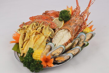 This image shows a seafood platter with a large lobster, mussels, squid, and crab, garnished with broccoli, corn, lemon slices, and carved carrot flowers.