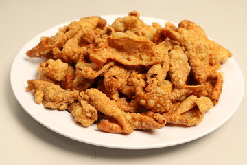 This image shows a white plate filled with crispy, golden-brown fried food that appears to be deep-fried chicken skin. The texture looks crunchy and bubbled. Let me know if you need more details!