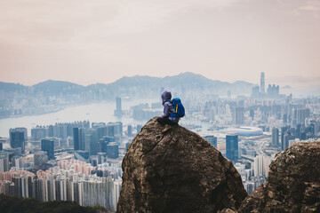 Woman traveller sit on the cliff edge enjoy the beautiful view of hong kong