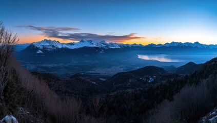 Panoramic winter sunrise over alpine peaks, valley, and lake.  Vast mountain range at dawn.  Snowy mountaintops meet a colourful sky