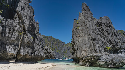 Picturesque karst cliffs by the ocean. Steep, furrowed slopes, sharp peaks against a clear blue sky. Filipino bangka boat is anchored in the sea. Philippines. Palawan. Secret lagoon.  Bacuit bay