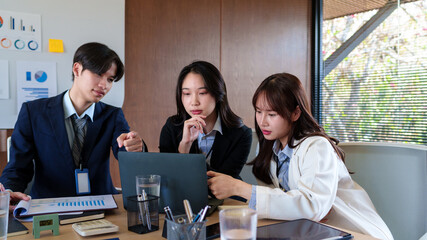 Young startup professionals discussing business data on a laptop, analyzing financial growth and marketing strategies in a modern collaborative workspace for innovative decision-making