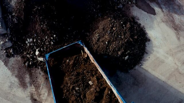 Aerial above view of a dumper tipping rocks and dirt into a pile. Drone shot with small pan down.