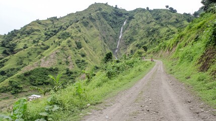 Fototapeta premium Gravel Road Winding Through Lush Green Mountains with Waterfall