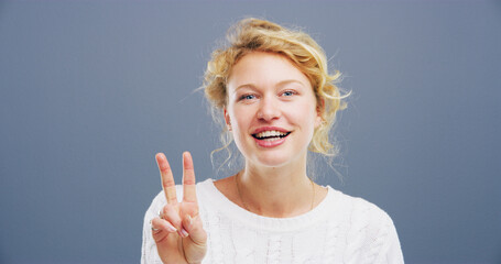 Woman, portrait and hand with peace sign in studio, icon or symbol for expression on blue...