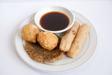 A plate of pempek (indonesian fish cake) with a variety of items including adaan (ball shaped), lenjer (long shape), and kulit (circle). The plate is set on a white background.