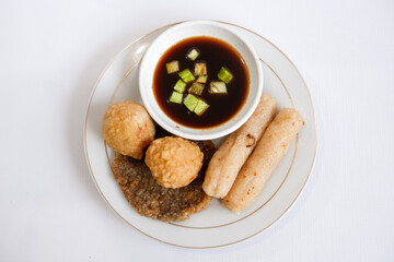A plate of pempek (indonesian fish cake) with a variety of items including adaan (ball shaped), lenjer (long shape), and kulit (circle). The plate is set on a white background.