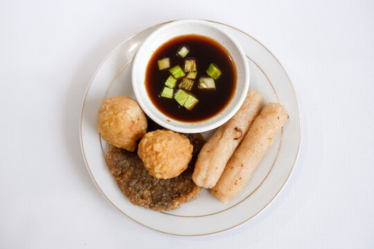 A plate of pempek (indonesian fish cake) with a variety of items including adaan (ball shaped), lenjer (long shape), and kulit (circle). The plate is set on a white background.