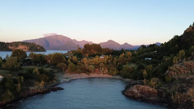 Aerial: sunset over Ranco Lake with trees and forest near Lago Ranco in Ranco Province, Los Rios Region, southern Chile, dolly in pan left drone shot