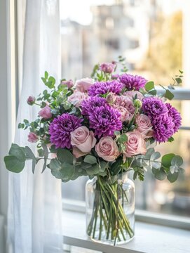 Beautiful arrangement of purple flowers and pink roses in a clear vase near a window showcasing natural light and a soft urban background