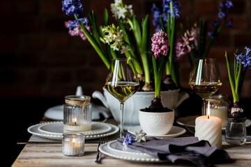 Beautiful elegant table setting for Easter celebration with fresh spring hyacinth flowers, burning candles. Romantic wedding dinner table decoration. Springtime, home gardening. Dark background