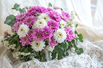 Beautiful bouquet of pink and white chrysanthemums arranged elegantly on a soft lace background with delicate green foliage adding charm to the floral display