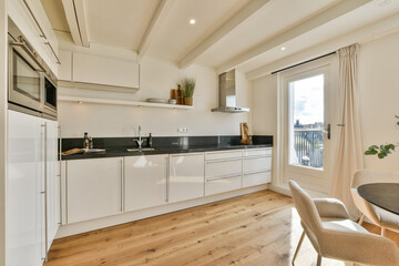A sleek, modern kitchen featuring white cabinets, a black countertop, and natural light streaming in through a large window, creating an inviting cooking space.