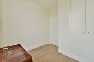 A modern interior showcasing a minimalist design with light colors, wooden flooring, and simple cabinetry. The space emphasizes simplicity and functionality.