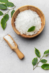 Magnesium flakes in wooden bowl with scoop and green leaves on marble background