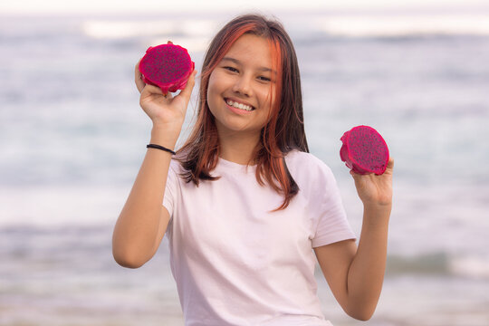 Portrait of attractive Asian teenager girl holding red dragon fruit halves. Outdoor photoshoot with dragon fruits. Bali.