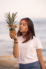 Close up portrait of teenager girl holding pineapple with sunglasses  in front of her face. Kissing lips. Closed eyes.
