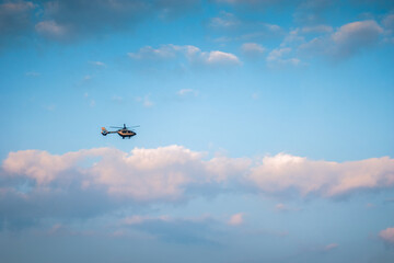 A helicopter flying high in the sky against a backdrop of blue sky and scattered clouds