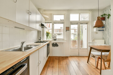 A bright and airy modern kitchen featuring minimalist design, wooden flooring, and natural light flowing through large windows, creating an inviting atmosphere.