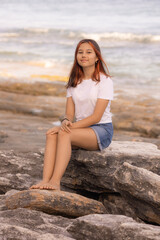 Beautiful teenager girl sitting on the stone on the beach. Summer vacation in Asia. Enjoy traveling to Bali island.