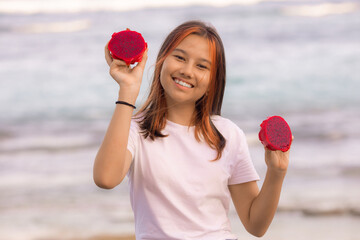 Portrait of happy Asian teenager girl holding red dragon fruit halves. Outdoor photoshoot with dragon fruits. Bali.