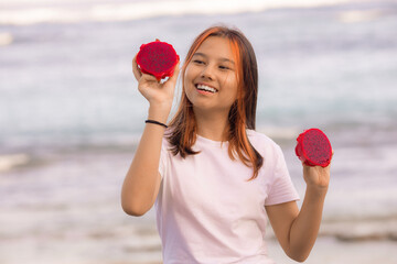 Portrait of beautiful Asian teenager girl holding red dragon fruit halves. Outdoor photoshoot with dragon fruits. Bali.